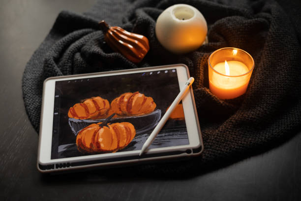 The still life picture with pumpkins drawn on the electronic tablet by digitized pen next to burning candle and ceramic pumpkin figurine on black table. la imagen de naturaleza muerta con calabazas dibujadas en la tableta electrónica junto a una vela encendida y una figura de calabaza de cerámica sobre una mesa negra. el concepto de inspiración, creatividad, autodesarrollo, hobby, arte moderno. hallowee