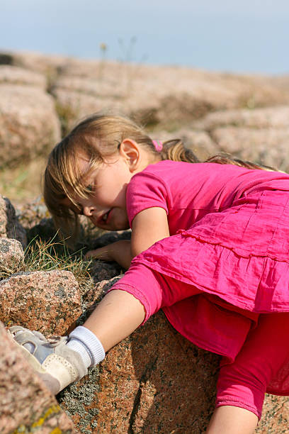A young girl sits on a man made rock to take a break at an outdoor park just watching the world pass by while a light summer breeze russles her hair during the summer.
