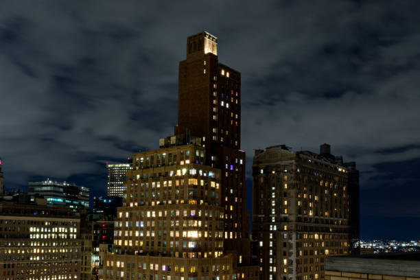 New York City buildings lit up at night with a moderately cloudy sky.