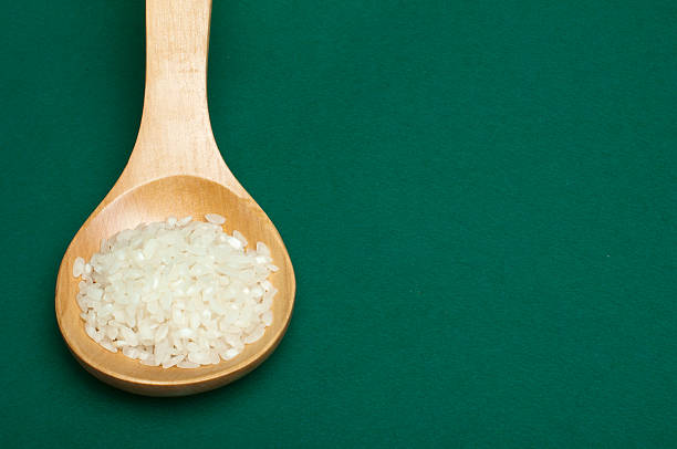 Rice baldo in wooden spoon on green background. Copy spice