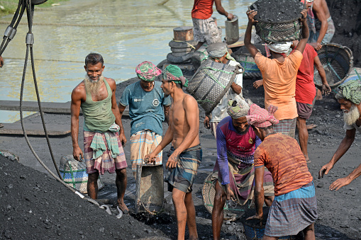 Chittagong,Bangladesh - December22,2022 - male worker is busy to loading a coal truck on his head . He is working without any safety equipment.