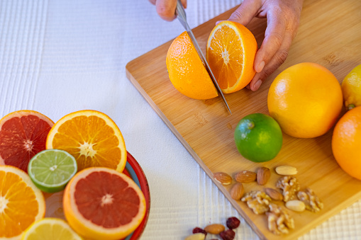 Group of whole and halved citrus fruits, wooden cutting board with female hand cutting an orange. Grapefruit, lime and dried fruit. Healthy eating concept