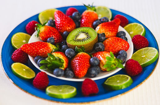 Close-up on a blue plate with fresh berries, strawberries raspberries blueberries and kiwi. Healthy nutrition and lifestyle concept