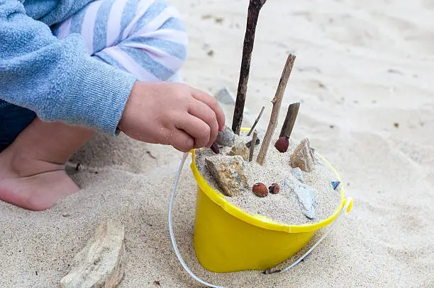 Photo of Child placing sand, rocks, shells, etc in a yellow bucket