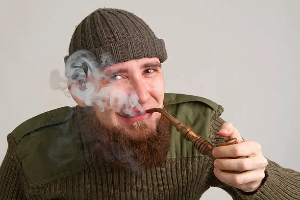 young bearded guy smoking a pipe on a light background