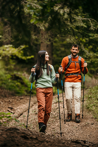 Fit couple briskly hikes a woodland trail with backpacks, embodying the perfect fusion of adventure and physical activity