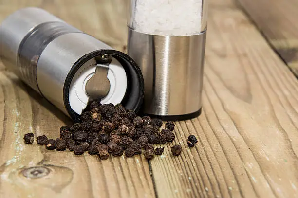 Peppershaker with Peppercorns on wooden background