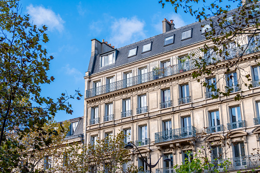 Facade of a classic-style residential building in Paris located on a tree-lined avenue. Concept of residential real estate market for old housing in France
