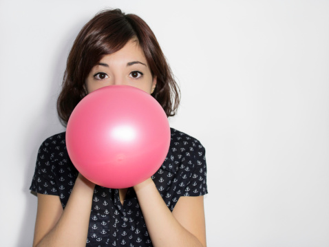 Portrait of a beautiful young woman blowing up a pink balloon on white background