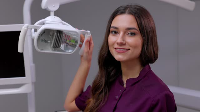 Caucasian female dentist turning on lamp before treatment, smiling to male patient
