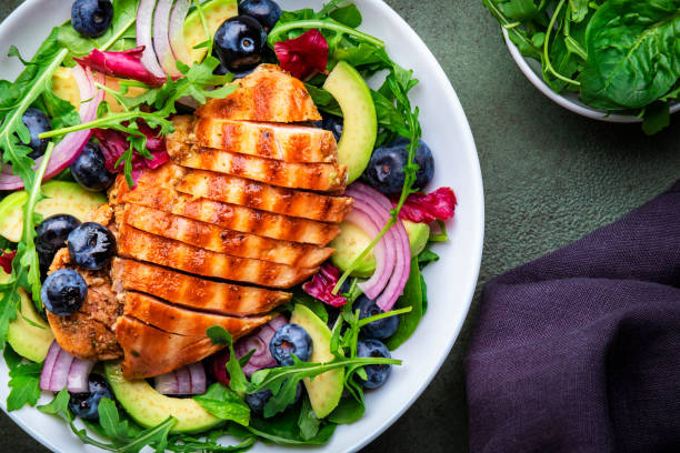 istock Fresh salad with blueberries, grilled chicken breast, avocado, red onion, walnuts and arugula on green table background, top view 1784413606