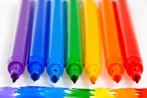 Top view of various crayons arranged side by side on a multicolored gradient on white background