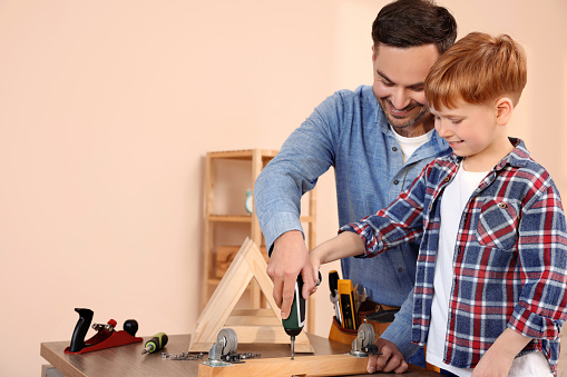 Father and son screwing wooden plank at home, space for text. Repair work