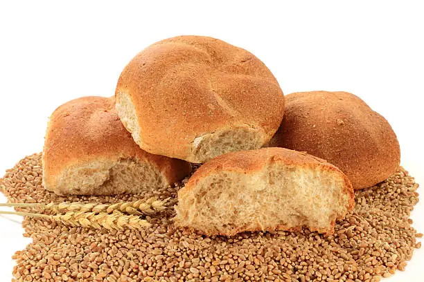 Pile Whole Wheat Buns and Ears of Wheat over Spilled Raw Wheat Kernels insolated on white background.