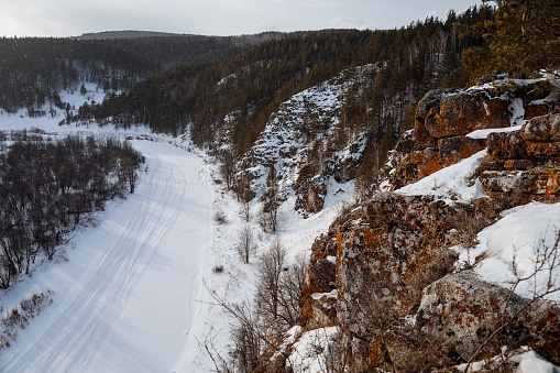 Winter view from the cliff to the river valley. A cold January landscape. Frozen river at the foot of the rocky mountains.