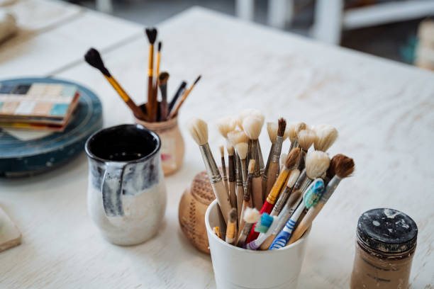istock Jars with brushes and other accessories for coating with ceramic glaze. On the table with a white tablecloth there are several cups and jugs. Creative pursuit. 1784447979