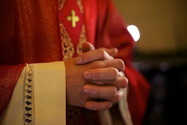 Catholic priest on altar praying with hands joined during mass service in church