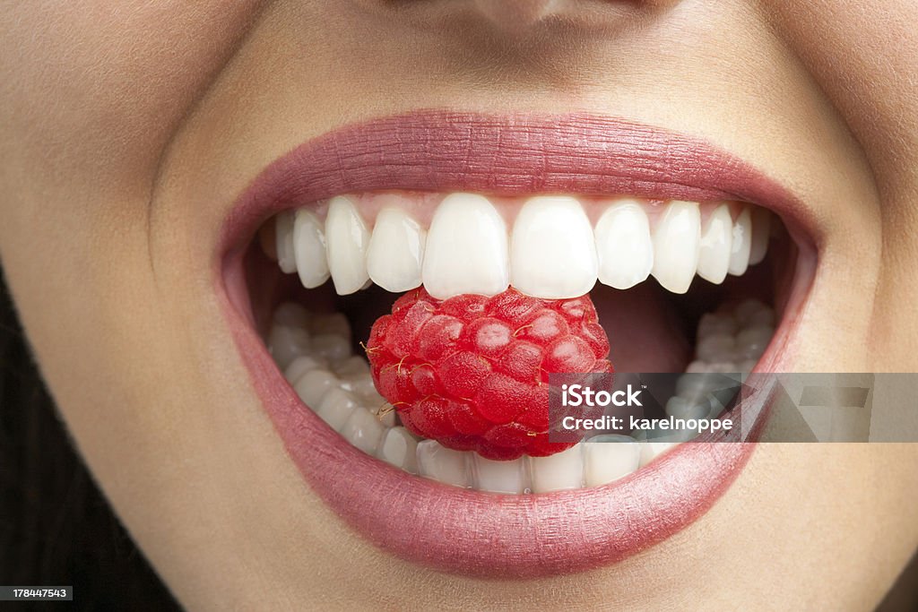 Perfect teeth biting raspberry. Macro close up of healthy female teeth biting raspberry. Raspberry Stock Photo