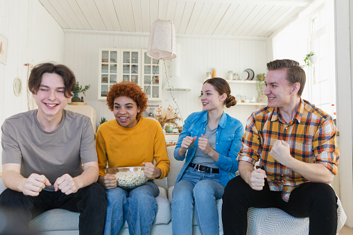 Group of friends watching sport match soccer football game on tv. Happy football fans celebrating victory at home. Friendship sports entertainment concept. Diverse buddies having fun together at home