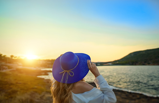 Woman in a blue hat at sunset by the sea.