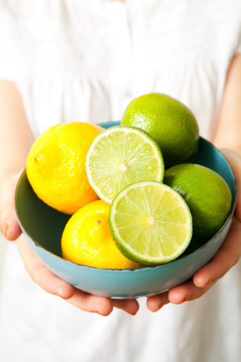 Various yellow and green type fresh ripe lemon fruits in a glass bowl. Group of organic lemons under sunny warm light with shallow depth of field. Pure antioxidant vitamin C. Natural food background with copy space.