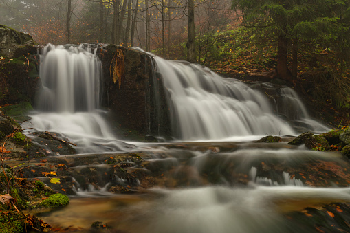 Ponikly waterfall with flood water after night rain in autumn foggy morning