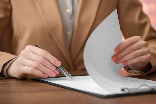 Woman signing documents at wooden table in office, closeup