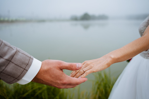 A close shot of the newlyweds, who stretch out their hands with rings to each other. Walk of the groom and the bride near the foggy lake. High quality photo