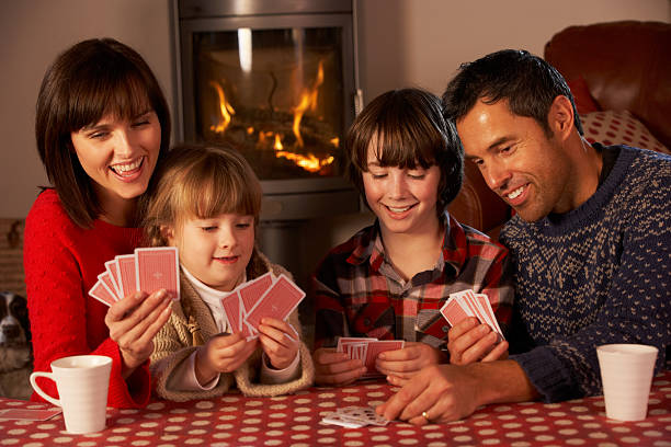 Portrait Of Family Playing Cards By Cosy Log Fire Portrait Of Family Playing Cards By Cosy Log Fire Sitting At Table Having Fun family playing card game stock pictures, royalty-free photos & images