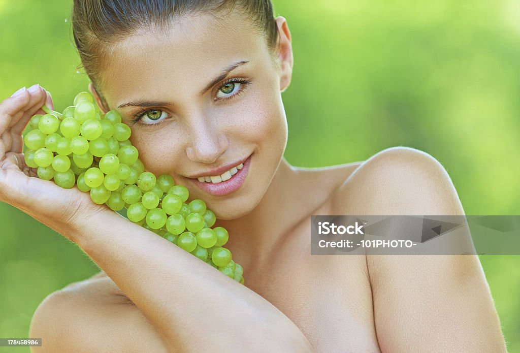 woman bites off from grape bunches Beautiful young woman bites off from grape bunches, against summer green park. Adult Stock Photo