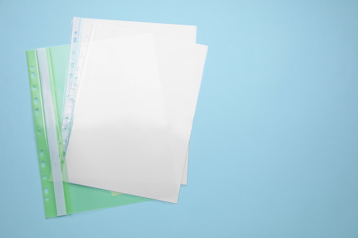 File folder with punched pockets and paper sheets on turquoise background, top view. Space for text