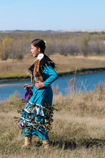 A teenage girl performing a First Nations Jingle Dress Dance along the riverbank in Saskatoon, Saskatchewan