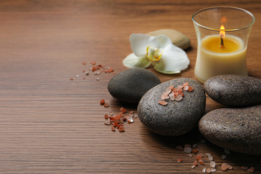 Beautiful composition with spa stones and burning candle on wooden table. Space for text