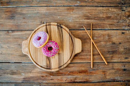 Kitchen utensils made of wood. Unusual photo. Bright pink doughnuts lying on a round wooden plate and Chinese sticks lying nearby, frame from above.. Plates made of natural material. High quality photo