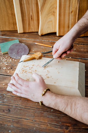Wooden utensils. A close shot of men's hands during the processing of a wooden rectangular surface. Sawdust is everywhere, wooden planks are exhibited at the back. Creation of high-quality and ecological tableware from wood independently. High quality photo