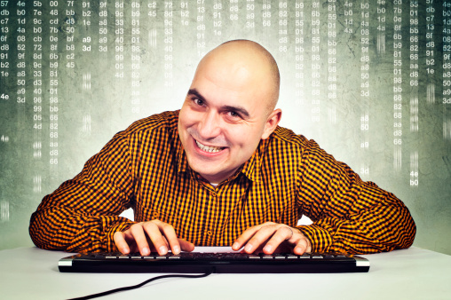 Bald young adult male computer hacker sitting at the table with keyboard in front of the monitor. Computer generated hex nubers in the background.