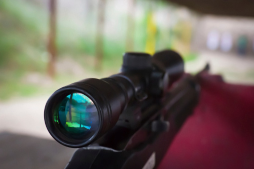 Angled view of rifle scope at a shooting range on AR 22 rifle resting on a red block.