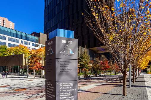 Cambridge, Massachusetts, USA - November 8, 2023: A directional sign post with arrows pointing to various buildings on MIT's East campus next to the Kendall Square Innovation District. Selective focus.