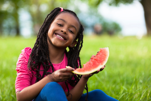 Outdoor portrait of a cute young black little  girl eating watermelon - African people