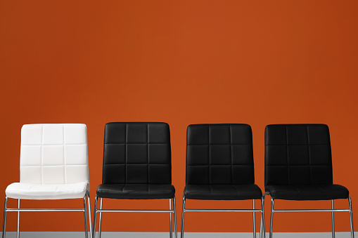 Black chairs with white one near orange wall, space for text. Recruiter searching employee