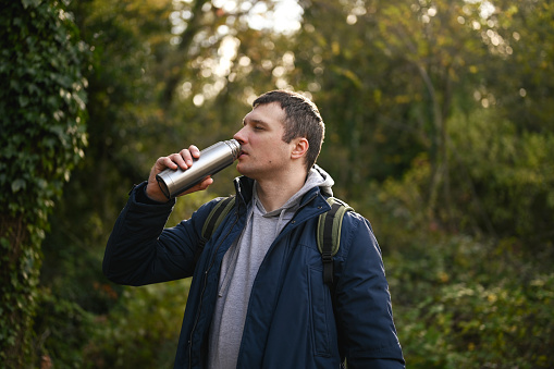 Hiking man drinking from steel drink container in a forest.