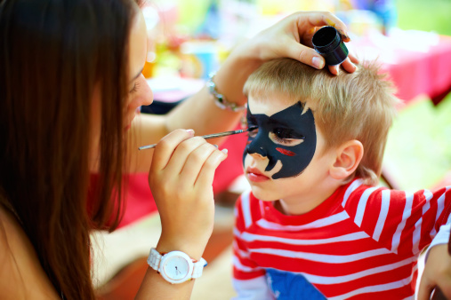 woman painting face of kid outdoors