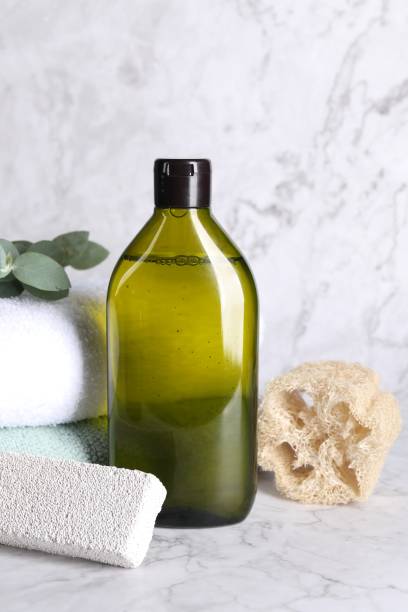 istock Shampoo bottle, loofah, folded towels and pumice on white marble table 1784628090