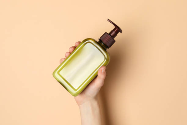 istock Woman holding shampoo bottle on beige background, top view 1784629694