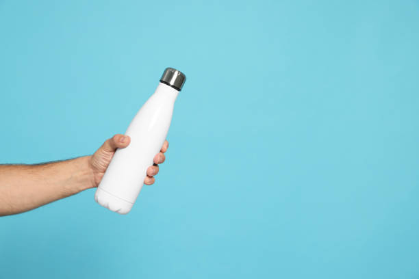 istock Man holding thermo bottle on light blue background, closeup. Space for text 1784638302