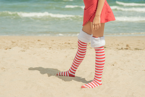 Legs' child girl wearing Santa Claus socks on beach near sea, legs and skirt. Xmas vacation High quality photo