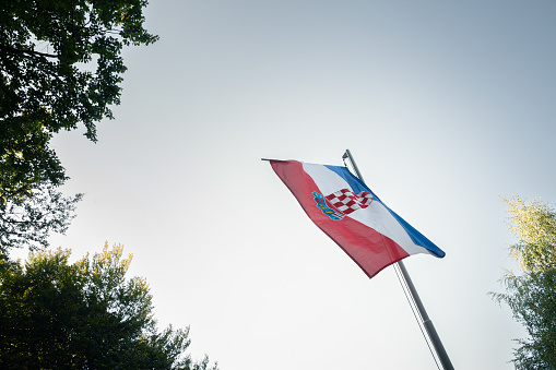 Picture of a Croatian flag flying in the air. The national flag of Croatia or The Tricolour is one of the state symbols of Croatia. It consists of three equal size, horizontal stripes in colours red, white and blue. In the middle is the coat of arms of Croatia.