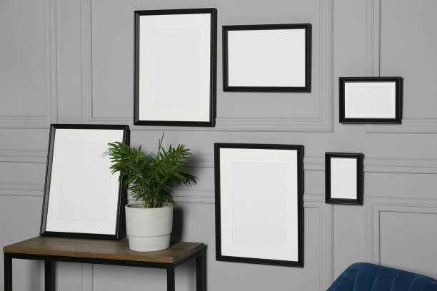 istock Empty frames hanging on grey wall near wooden table indoors 1784656340