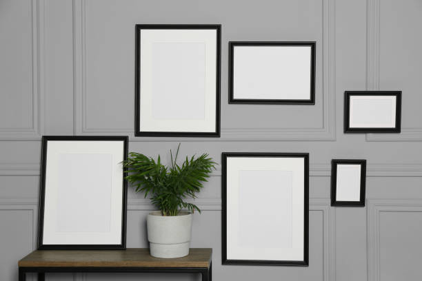 istock Empty frames hanging on grey wall near wooden table indoors 1784656358
