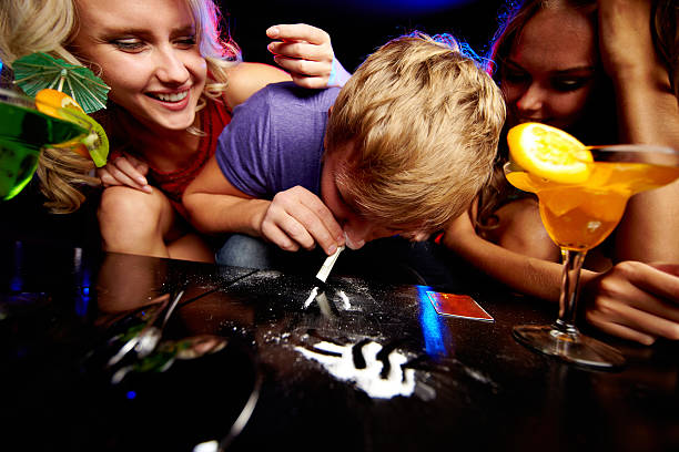 Addicted to cocaine Image of young guy sniffing cocaine surrounded by two girls in night club cocaine stock pictures, royalty-free photos & images